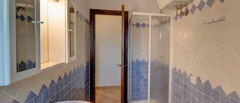 Baño con lavamanos, espejo, ducha y paredes con azulejos.