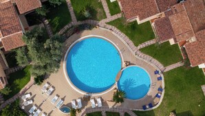 Vue aérienne d’un quartier résidentiel avec deux piscines, entourées de chaises longues et d’une pelouse bien entretenue.