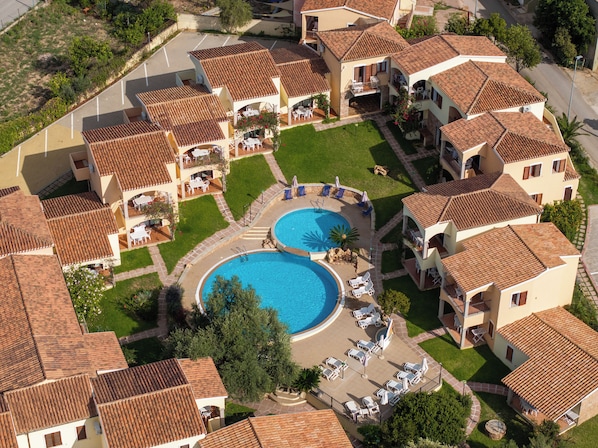 A residential complex with two swimming pools, multiple balconies, and a well-maintained lawn.