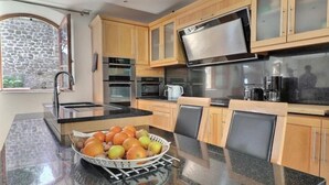 A modern kitchen with wooden cabinets, a stainless steel range hood, and a bowl of fruit on the counter.