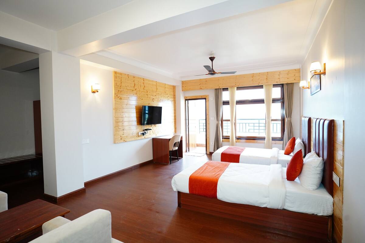 A hotel room with two beds, a desk, a TV, and a balcony with a view.