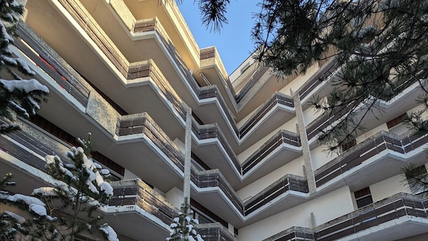 A multi-story building with a stone wall and snow-covered steps leading to the entrance. - Attic apartment 2 minutes from the center, with a dream terrace (Leukerbad)