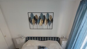 A neatly arranged bedroom with a large bed, a decorative wall piece, and a window with curtains. - Attic apartment 2 minutes from the center, with a dream terrace (Leukerbad)