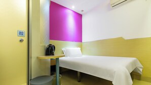 A small hotel room with a bed, a table with a kettle, a trash bin, and a wall with a bright pink accent. - YIbaihotel (Shanghai)