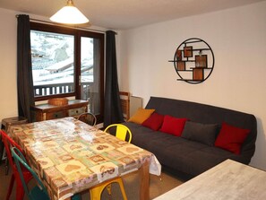 Un salon chaleureux avec un canapé, une table à manger et une vue sur un paysage enneigé par la fenêtre.