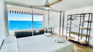 Une chambre avec un grand lit, un ventilateur de plafond, une vue sur l’océan et un plancher en bois.