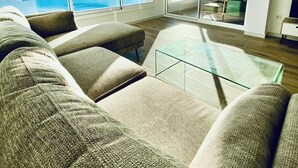Un salon moderne avec de grandes fenêtres, une table basse en verre et une vue sur l’océan.
