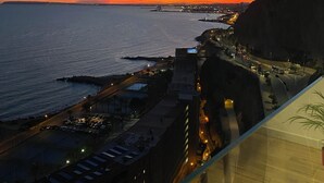 Un paysage urbain côtier au crépuscule, avec une vue sur la mer, un pont et des bâtiments le long de la côte.