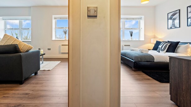 Ein modernes Wohnzimmer mit einer Couch, einem Bett und einem Couchtisch. Fenster bieten Ausblick nach draußen.
