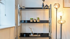 Ein modernes Interieur mit einem schwarzen Metallregal, das Pflanzen, eine Vase, einen gewebten Korb und eine Stehlampe mit einer Kugelform zeigt.