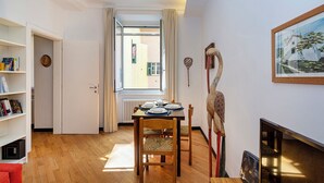 Ein gemütliches Zimmer mit Holzboden, einem Esstisch für zwei Personen, einem Bücherregal und einem Gemälde an der Wand.