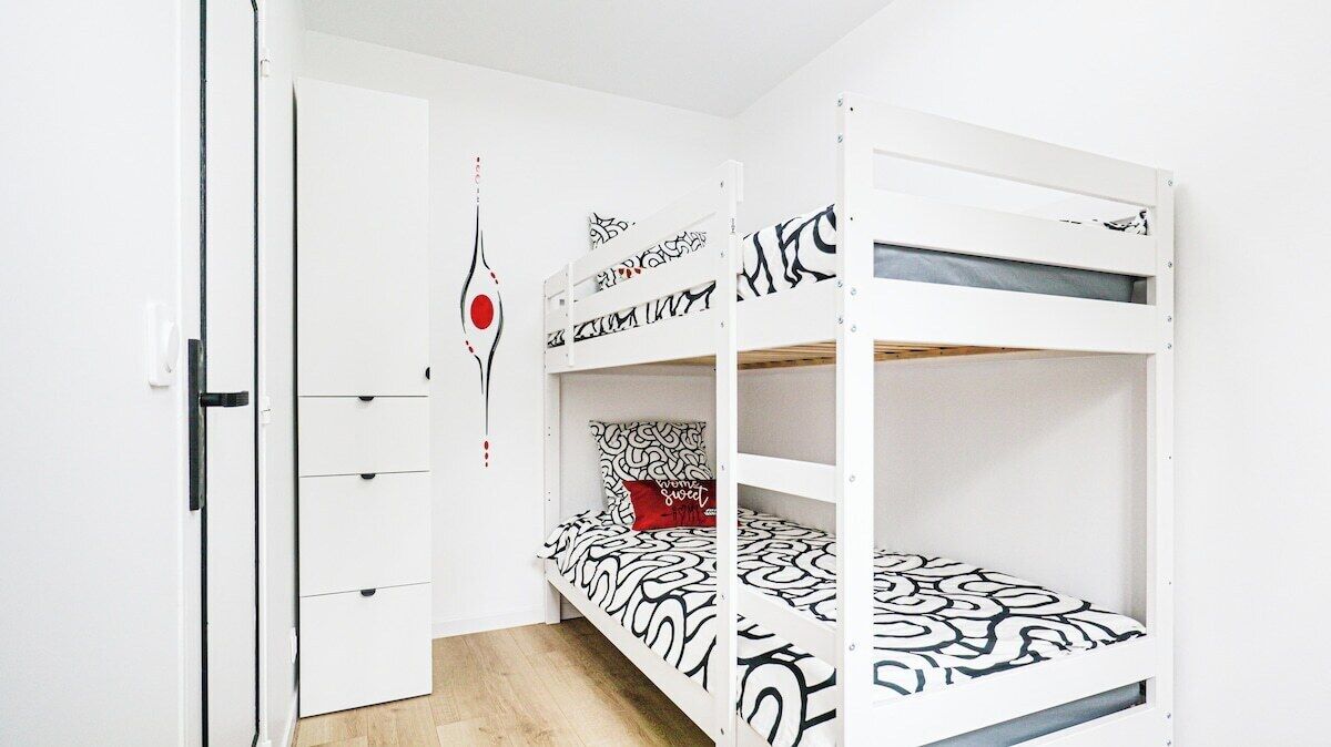 Un lit superposé avec une couvre-lit à motifs, un oreiller rouge et une décoration murale.