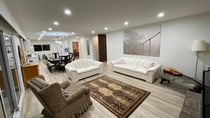 Ein modernes Wohnzimmer mit zwei weißen Sofas, einem gemusterten Teppich und einem Essbereich mit Tisch und Stühlen.