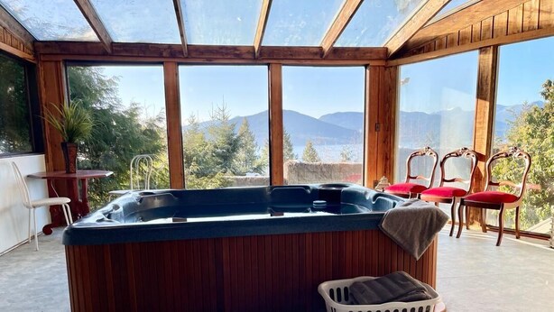 Ein Whirlpool in einem Zimmer mit großen Fenstern, Holzwänden und Blick auf Berge.
