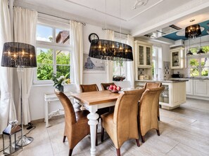 Uma sala de jantar com mesa e cadeiras de madeira, um lustre e vista para o verde lá fora.