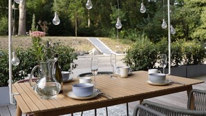 An outdoor dining area with a wooden table set for four, surrounded by wicker chairs.