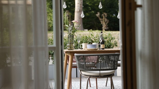 An indoor dining area with a table set for two, featuring a vase with flowers and a bottle.