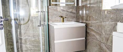 A modern bathroom with a glass shower enclosure, a white sink with a gold faucet, and a marble-tiled floor.