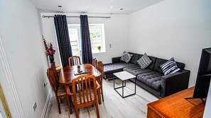 A modern living room with a dining table, sofa, and TV. - Modern 4-Bedroom Home with Free Parking (Slough)