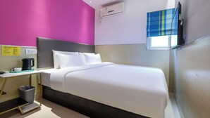 Une chambre d’hôtel avec un lit, une table de chevet, une machine à café, une poubelle et une fenêtre avec un rideau bleu.