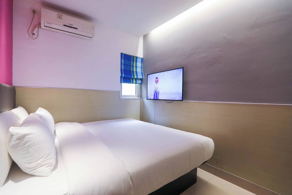 Habitación de hotel con cama, televisor montado en la pared y unidad de aire acondicionado en el techo.
