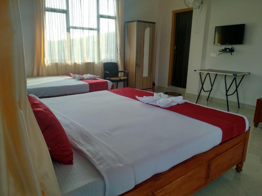 A hotel room with two beds, a desk, a wardrobe, and a TV.
