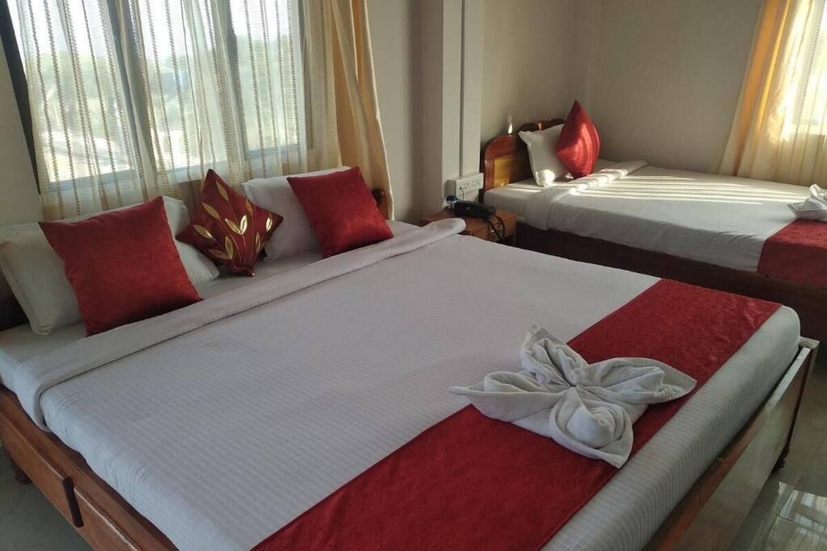 A hotel room with two beds, each with white linens and red accents, and a neatly made bed with a white towel.