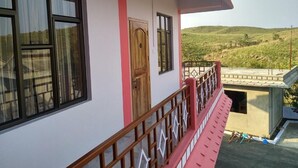A building with a balcony, a wooden door, and a view of a hilly landscape. - Sulawado Resort (Shillong)