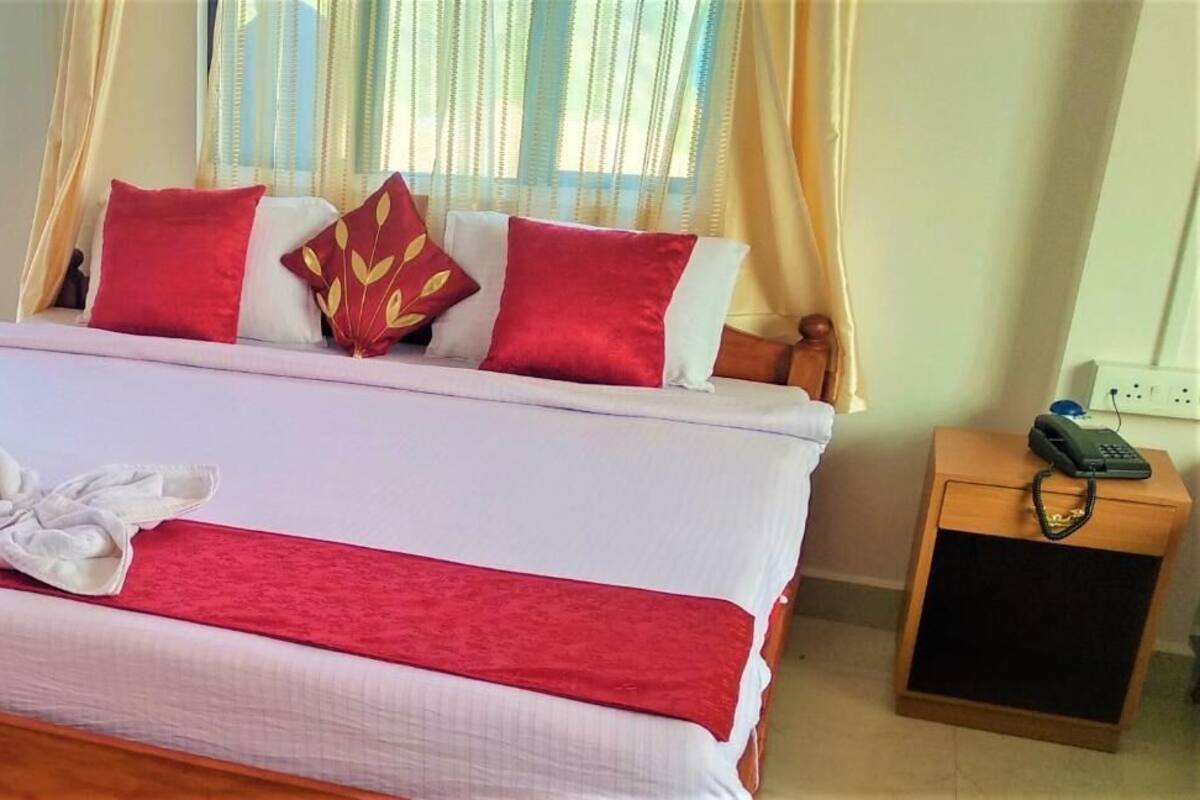 A neatly made bed with red and white bedding, a wooden nightstand with a telephone, and sheer curtains.