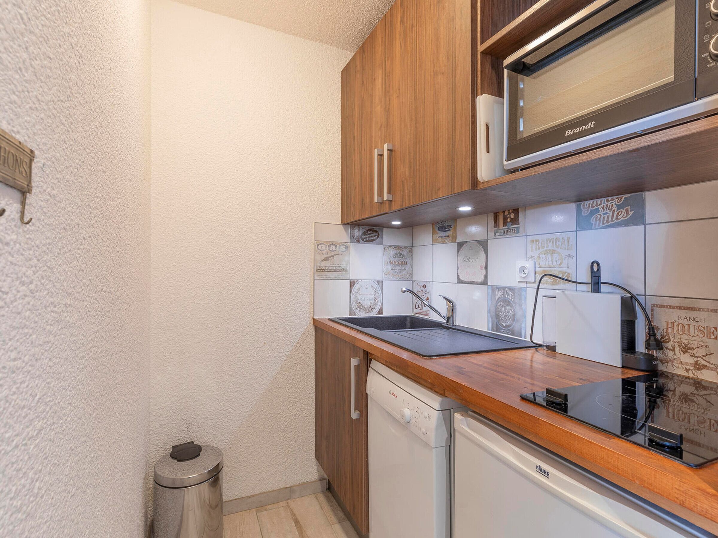 A compact kitchen with wooden cabinets, a built-in microwave, and a dishwasher.