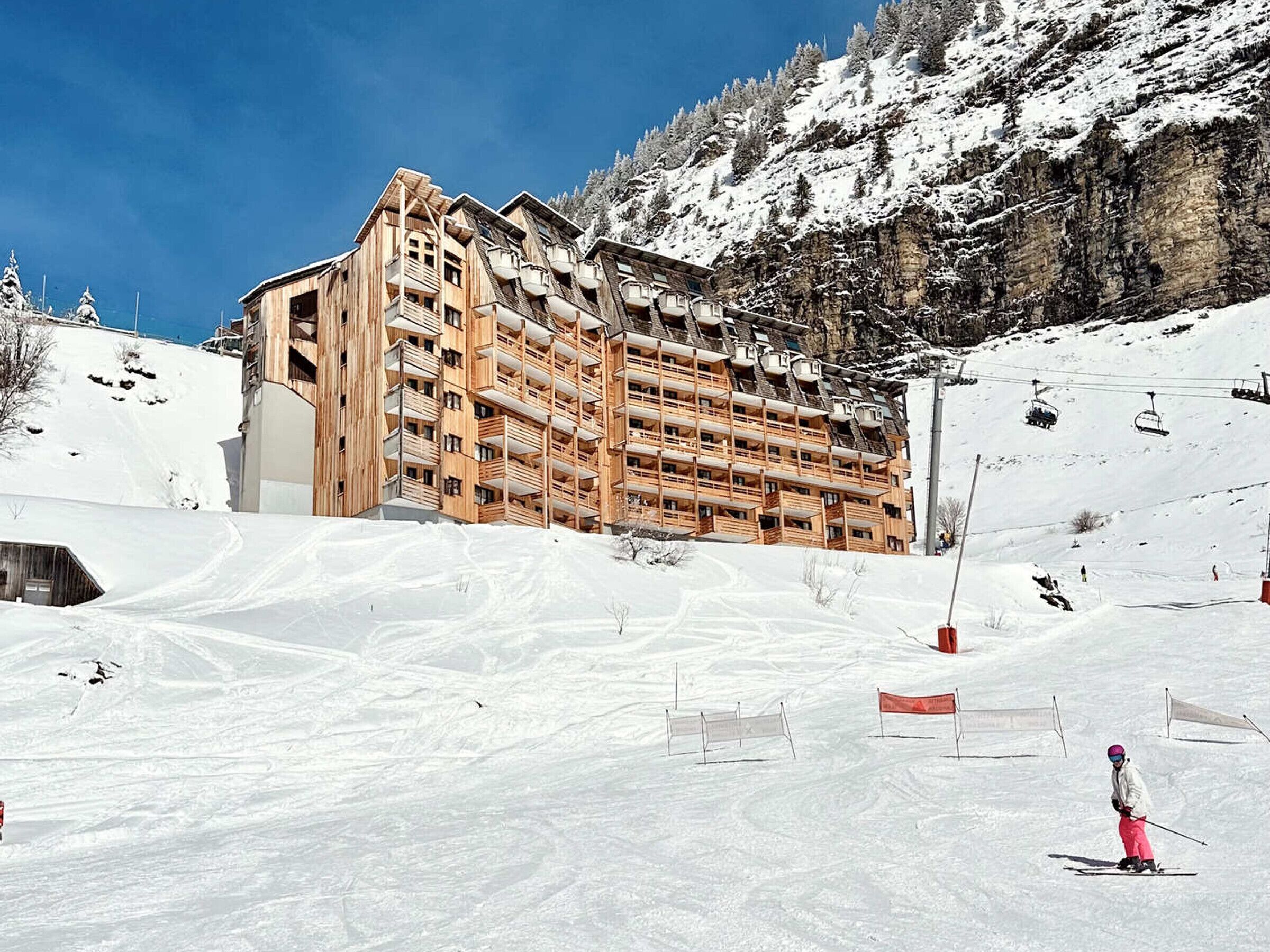 Un immeuble en bois à plusieurs étages, doté de balcons, se dressant sur fond de montagnes enneigées.