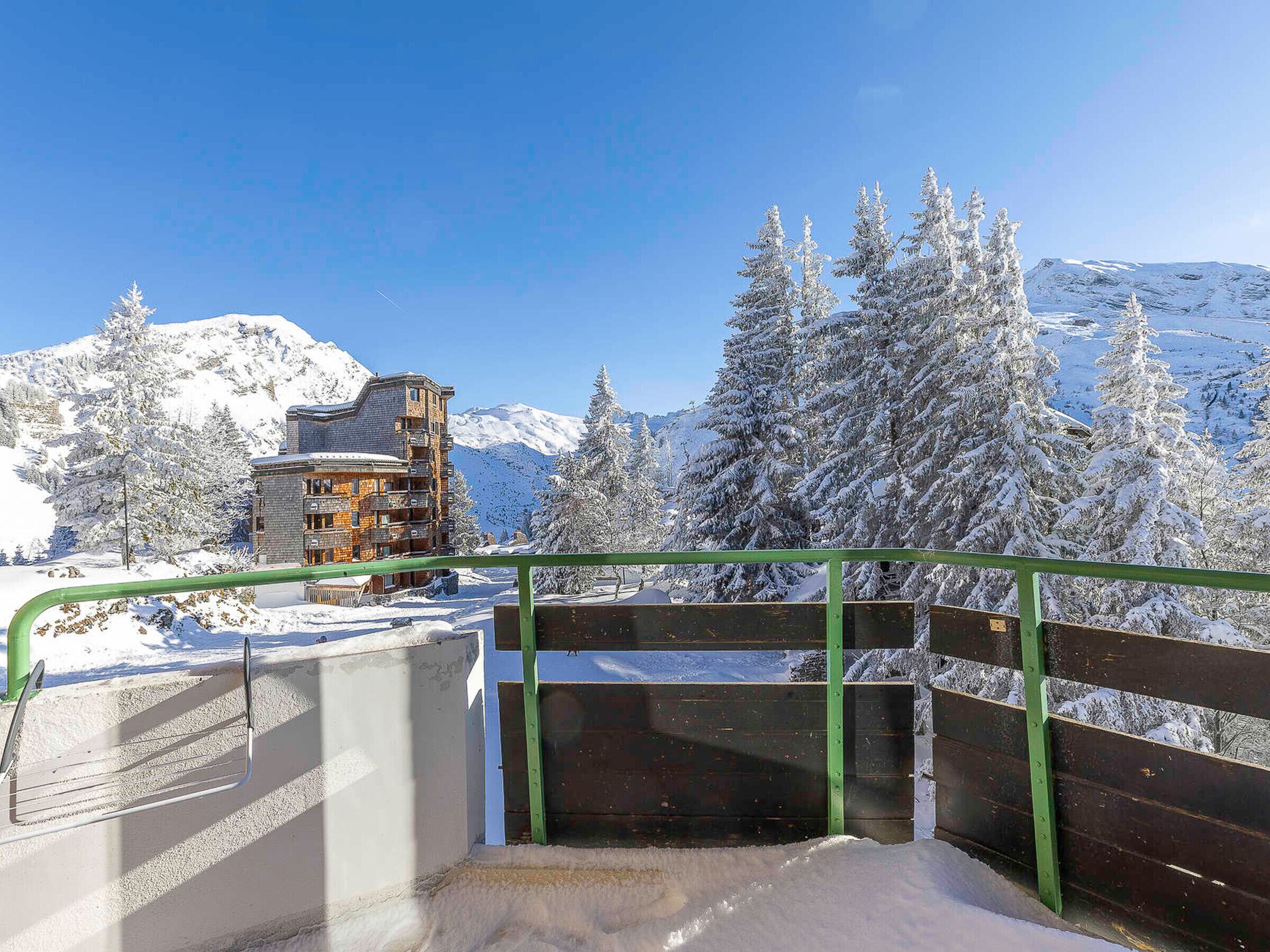 A snow-covered mountain landscape with a wooden building and a green railing in the foreground.