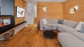 A modern living room with a fireplace, a sofa, a round coffee table, and wooden paneling on the walls.