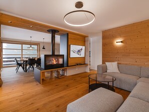 Een moderne woonkamer met een open haard, houten vloeren, een bank, een glazen salontafel en een eethoek met een tafel en stoelen.