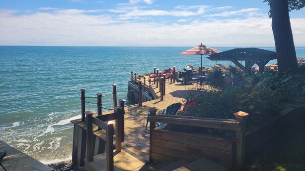A wooden deck leading to a beach with a grill and outdoor seating.