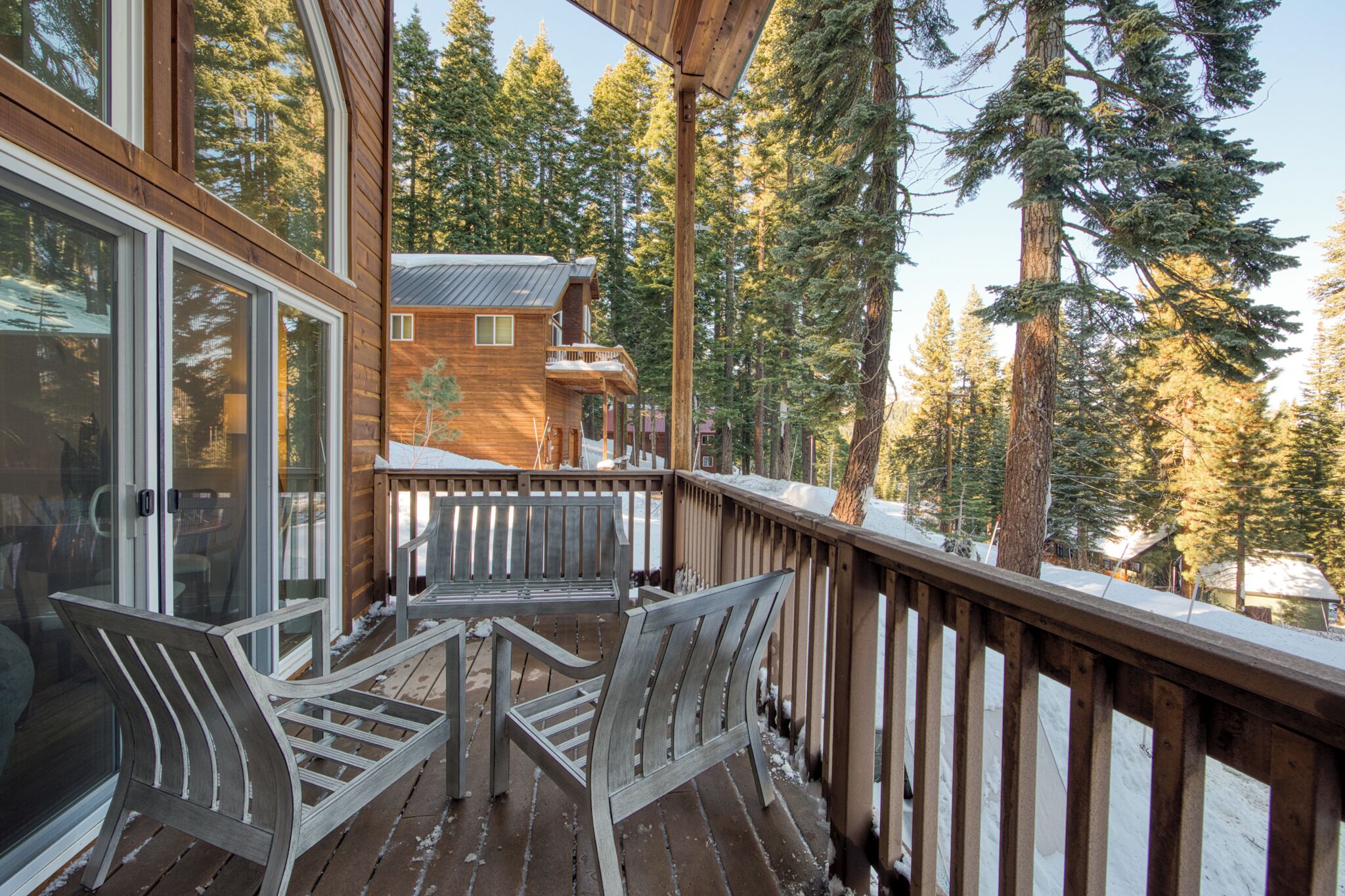 A wooden deck with two chairs and a table, overlooking a forested area with tall trees.