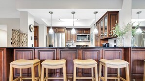 A kitchen with wooden bar stools, stainless steel appliances, and pendant lighting.