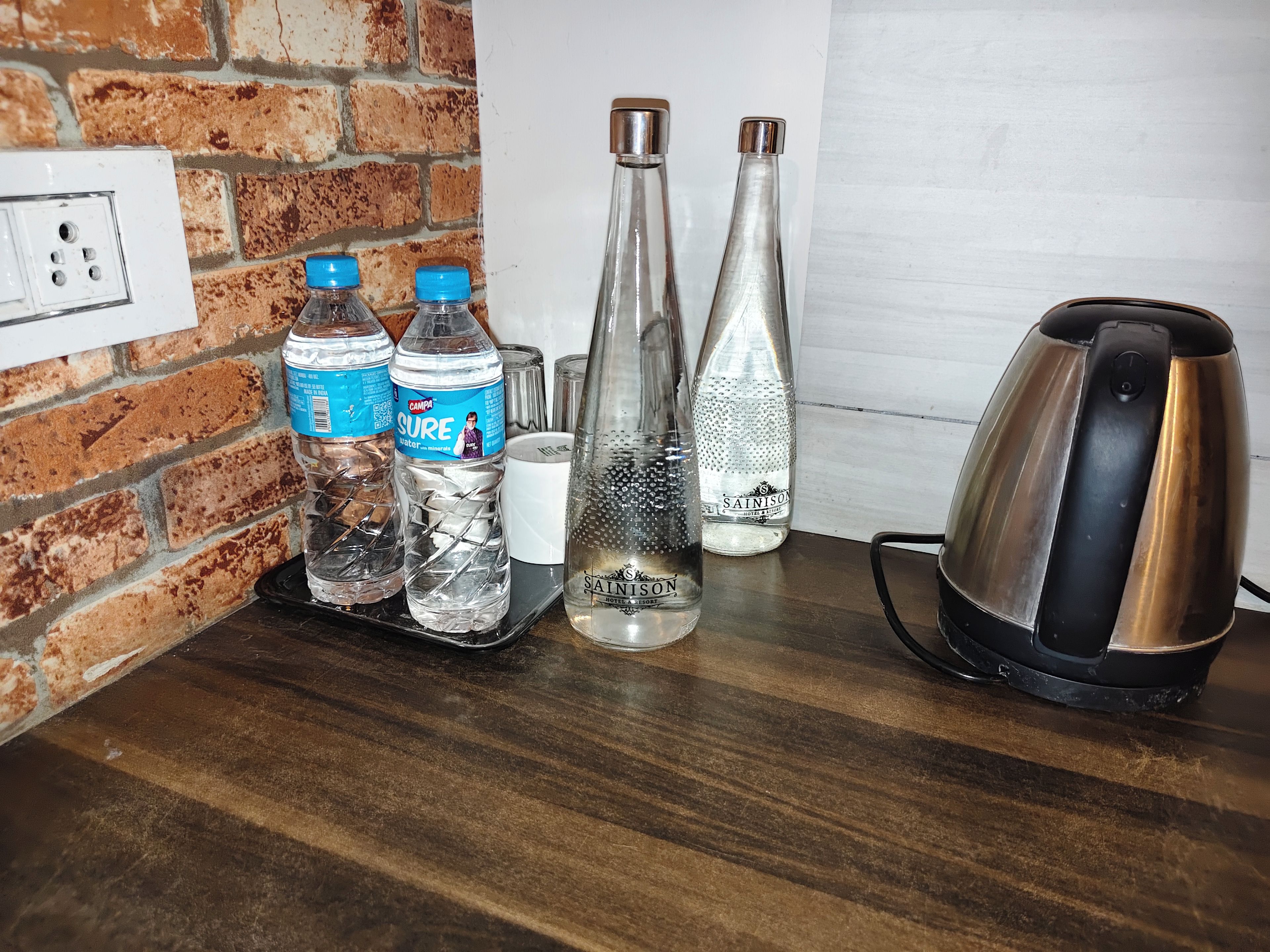 A kitchen counter with two water bottles, a glass bottle, a white mug, and a kettle.