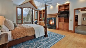 A bedroom with a large bed, a fireplace, a ceiling fan, and a TV.