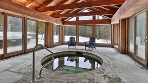 A spa area with a hot tub, wooden beams, and large windows overlooking a snowy landscape.