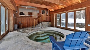 A wooden interior with a stone hot tub, a staircase, and a view of the outside.