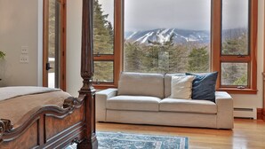 A bedroom with a four-poster bed, a beige sofa with pillows, and large windows offering a mountain view.