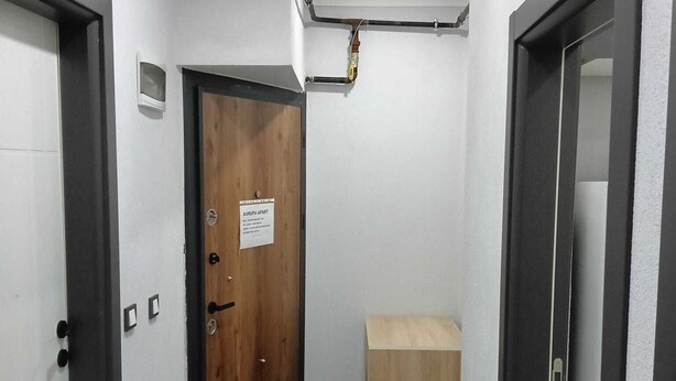 A narrow hallway with a wooden door, a small wooden cabinet, and a patterned rug. - AVRUPA Suit - otel (Bandirma)