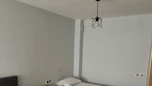 A bedroom with two beds, a wooden nightstand, a ceiling light fixture, and a small rug. - AVRUPA Suit - otel (Bandirma)