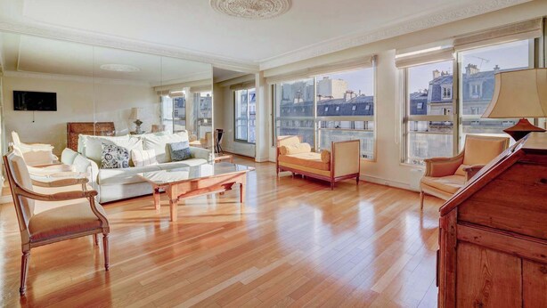 A spacious living room with a large window, a sofa, a coffee table, and a wooden cabinet.