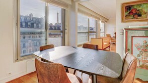 A dining area with a large table, chairs, and a view of a cityscape through large windows.