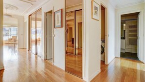 A spacious hallway with wooden flooring, a sliding glass door leading to a balcony, and a laundry room with a washing machine.