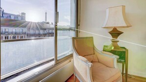A room with a large window overlooking a cityscape, a chair, and a table with a lamp.