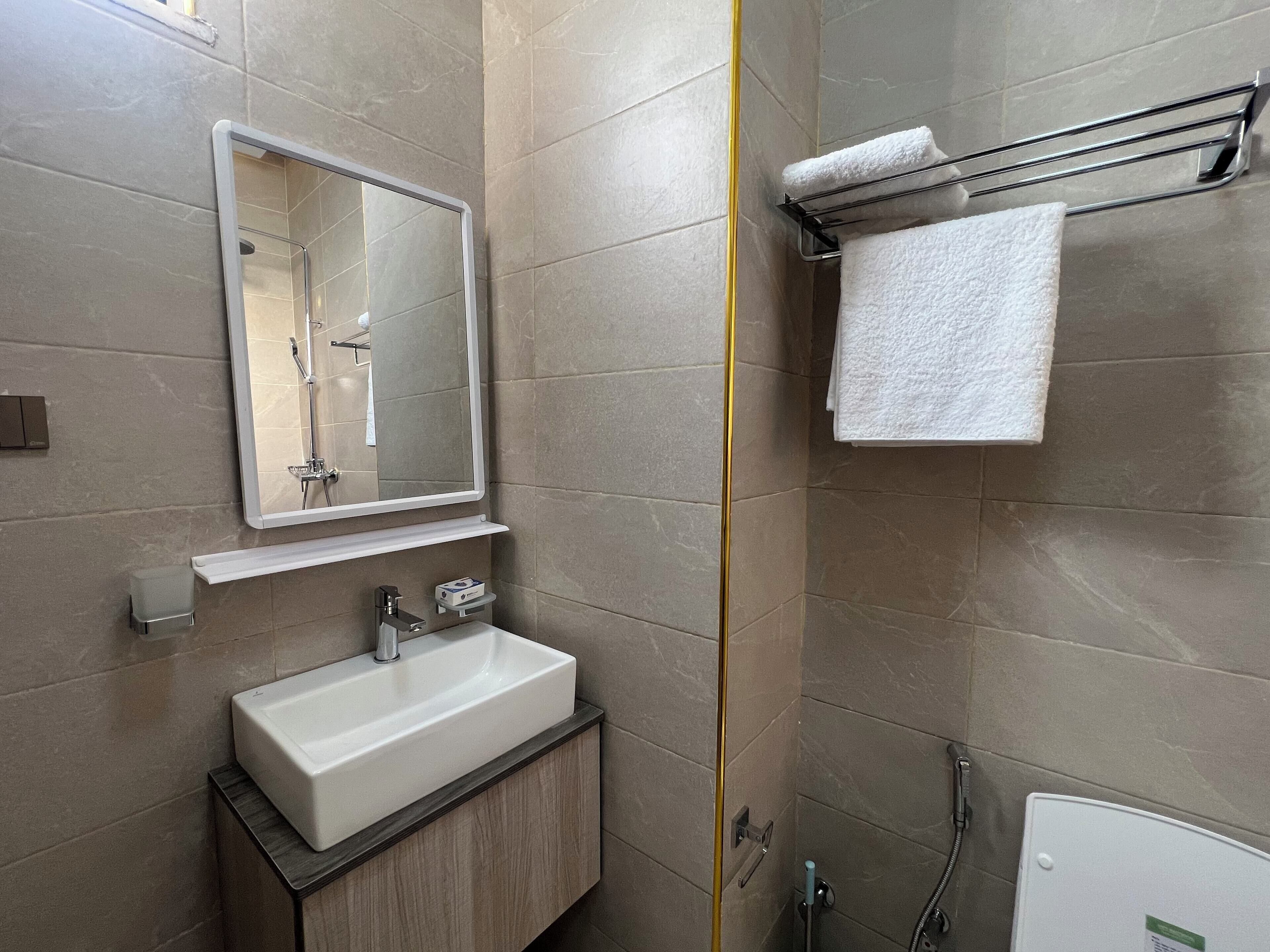A modern bathroom with a large mirror, a sink, a towel rack, and a shower.