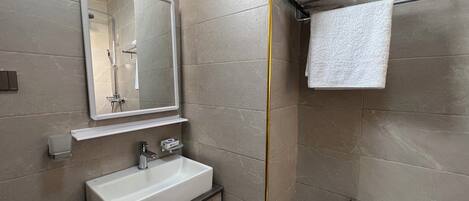 A modern bathroom with a large mirror, a sink, a towel rack, and a shower.
